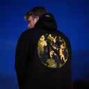 Person wearing a black hoodie with a camouflage pattern on the back against a dark blue sky.