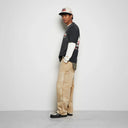 Person wearing a black and white outfit with beige pants against a plain background