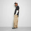 Person wearing a black and white outfit with beige pants against a plain background